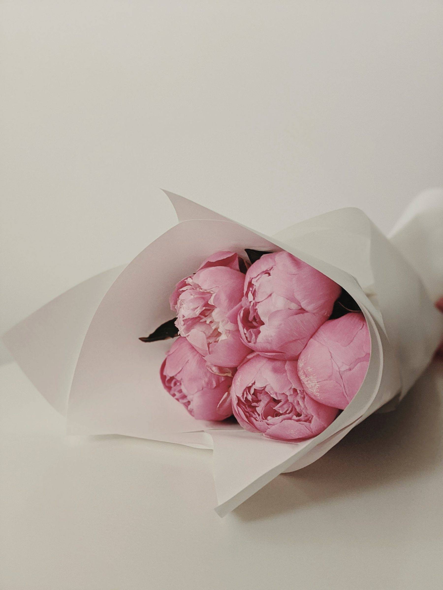 A bouquet of pink peonies wrapped in soft white paper