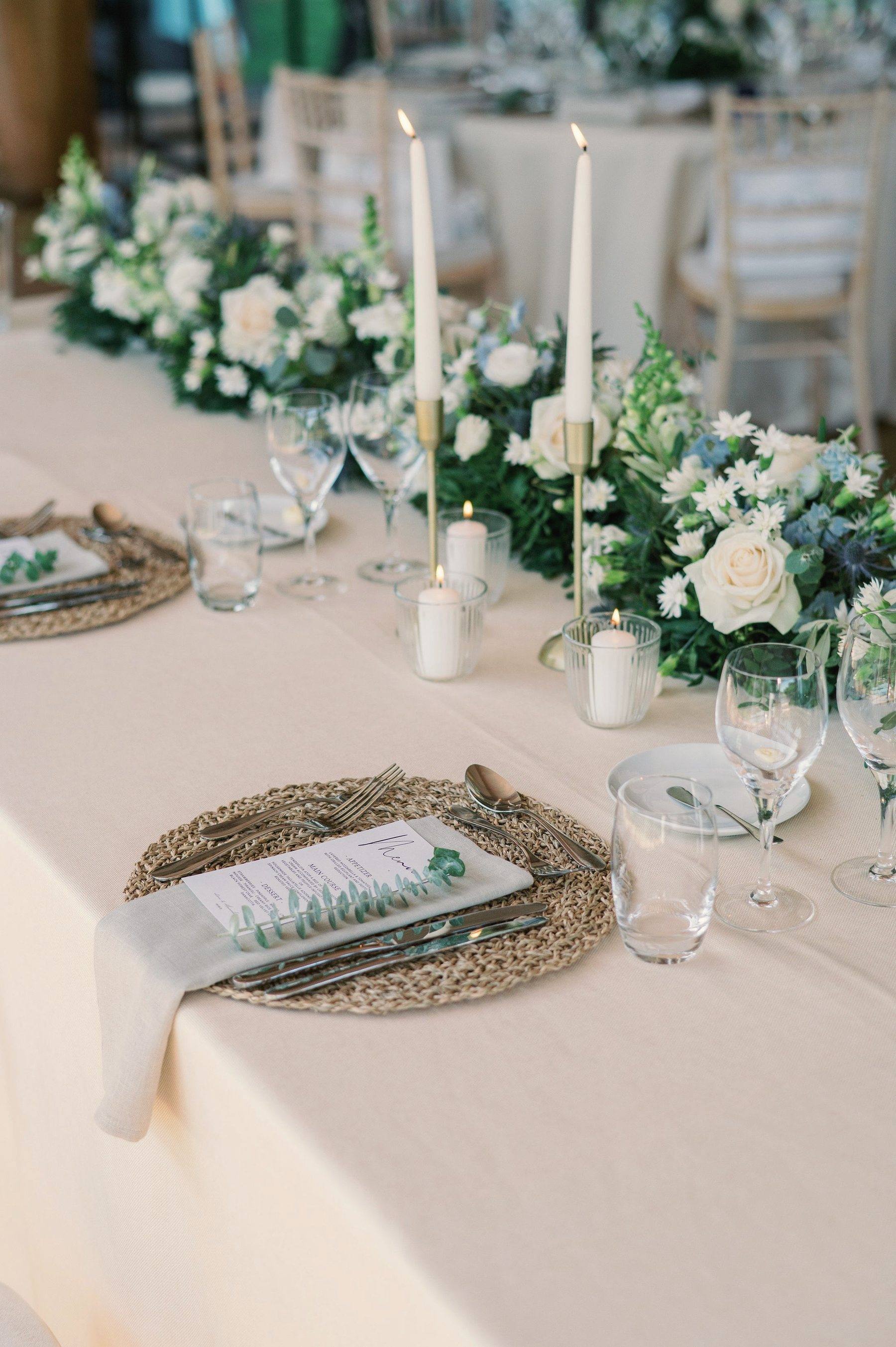 A long table dressed in linen with cream flowers, eucalyptus and tall candles