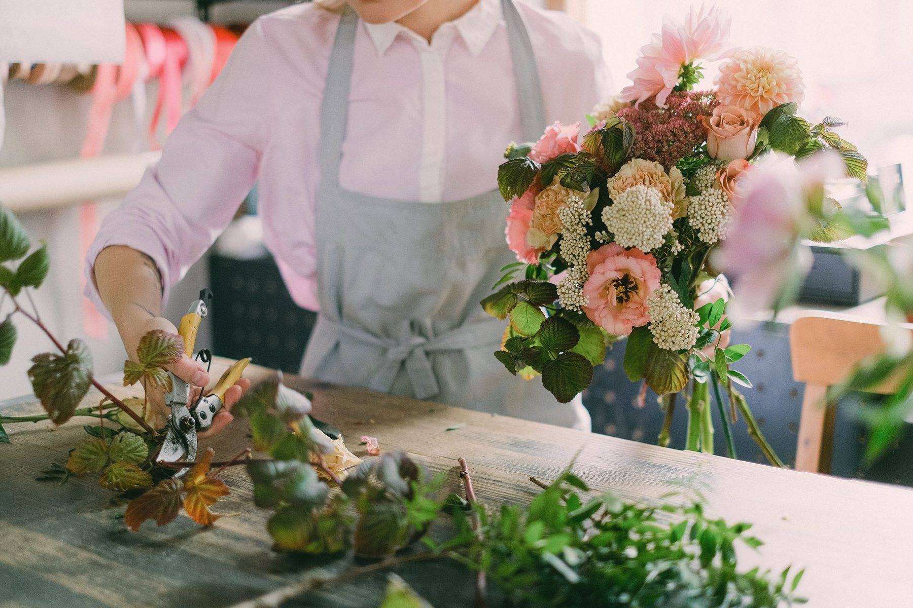 A finished bouquet of peach and blush flowers beside the work table
