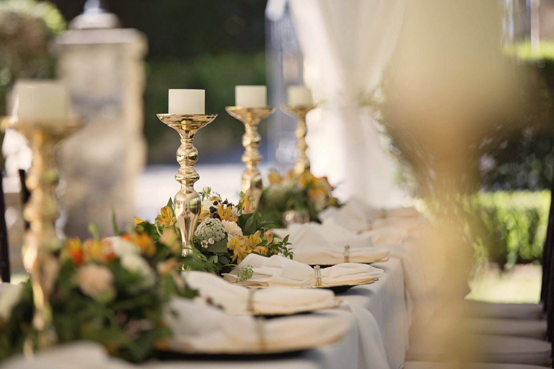 An outdoor table set with gold candlesticks and flowers