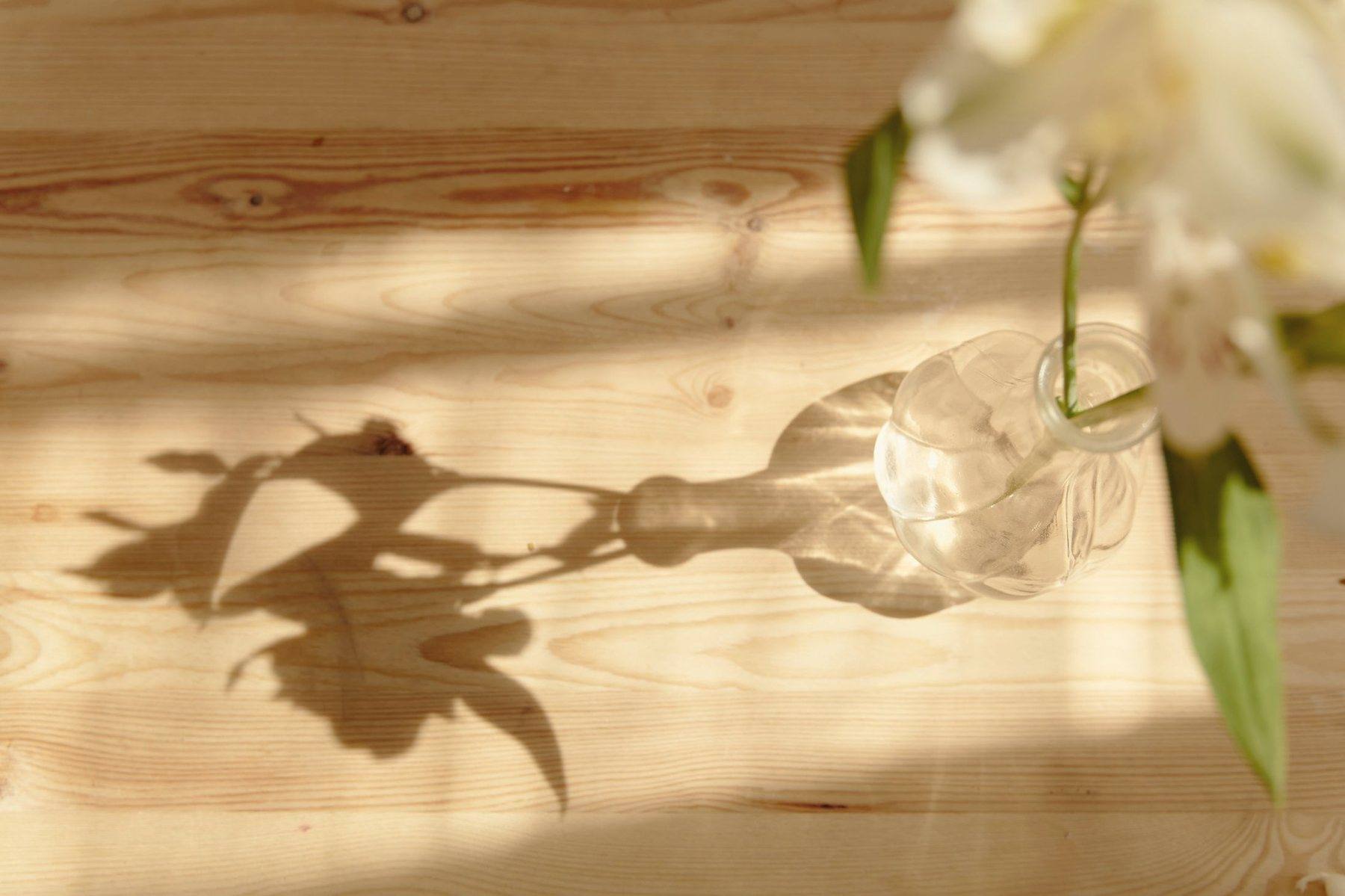 The shadow of a vase of flowers falling across a wooden table