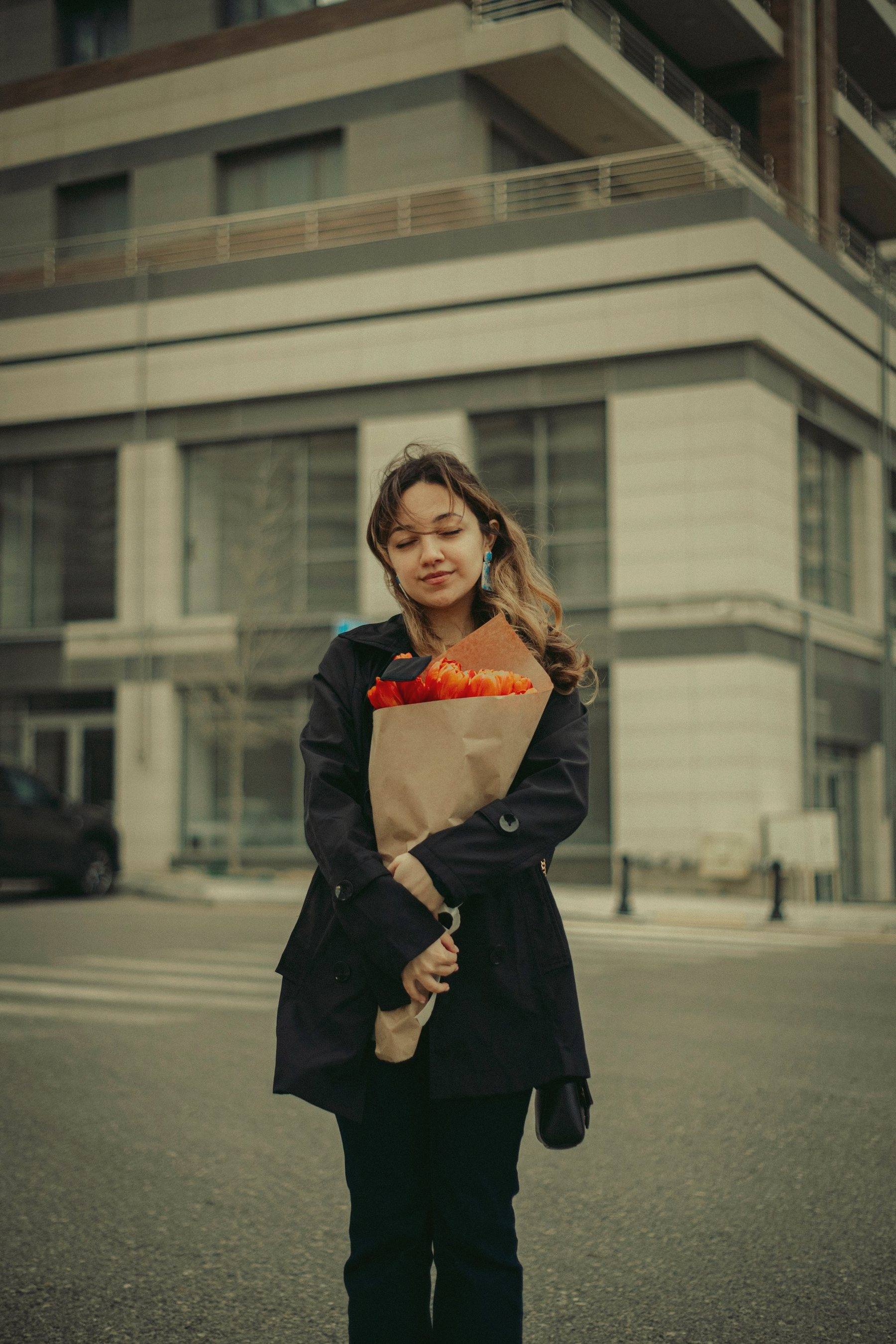 A woman on a city street holding a wrapped bouquet