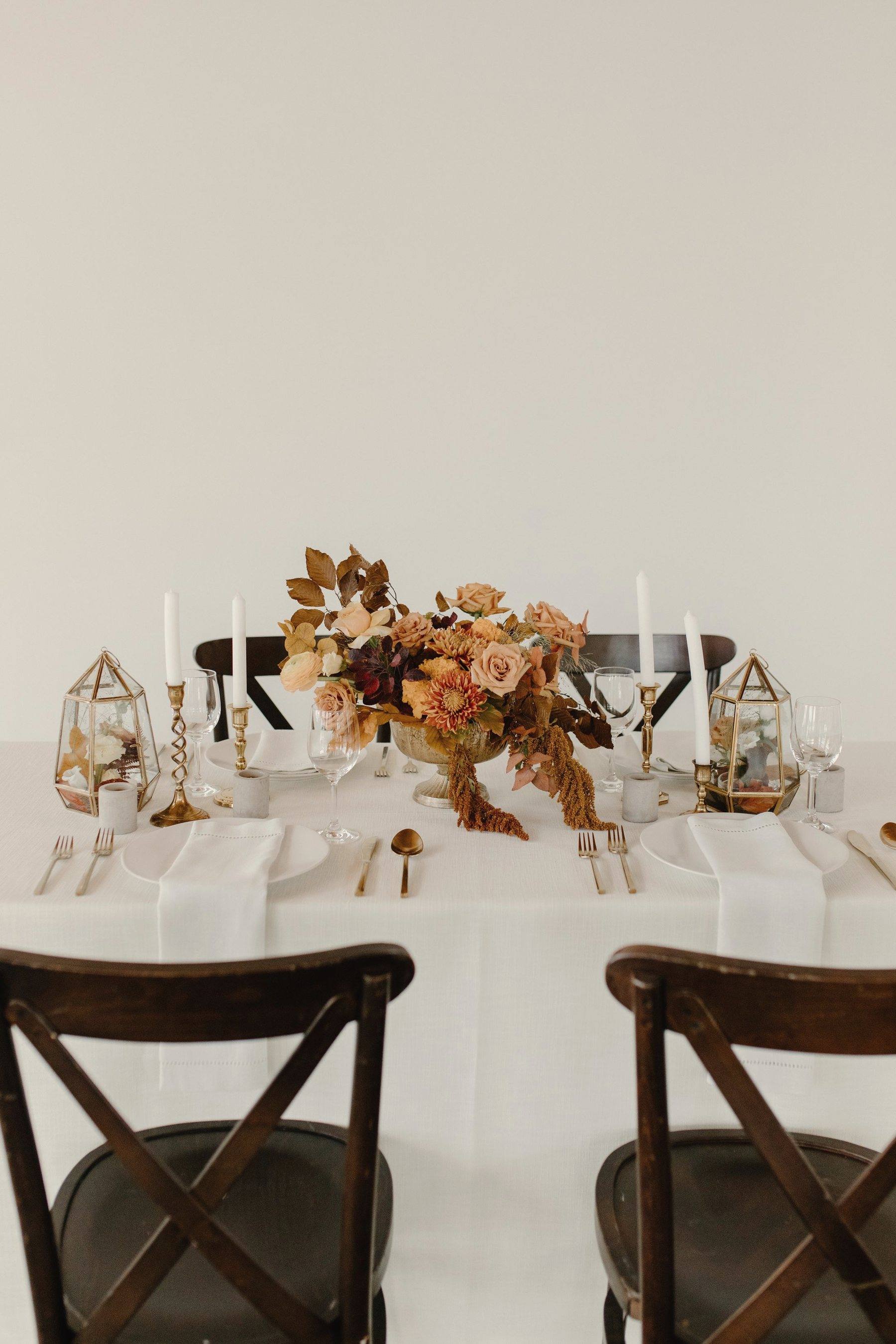A dinner table set for a celebration with a low autumnal floral arrangement