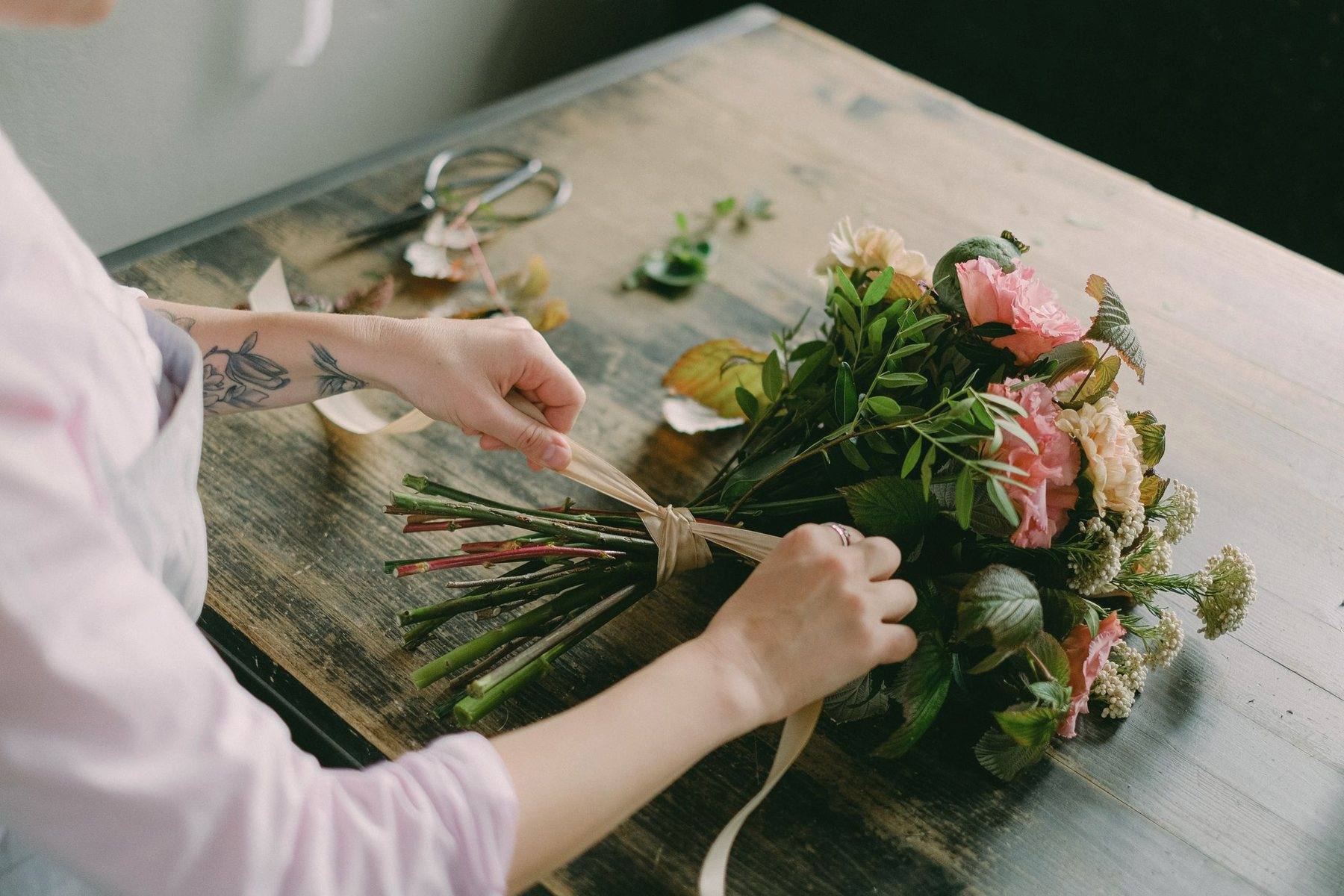 Hands tying a garden-style bouquet on a wooden workshop table